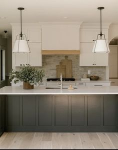 a large kitchen with white cabinets and gray island counter tops, along with two hanging lights over the sink