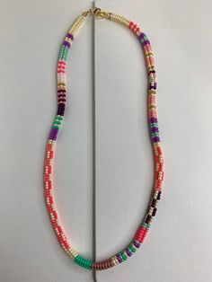 a multicolored beaded necklace on a white surface with a gold hook clasp