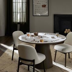 a dining table with four chairs around it in front of a fireplace and pictures on the wall