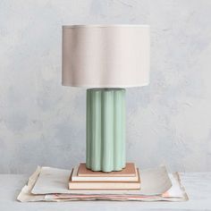 a green lamp sitting on top of a table next to a stack of papers and a white lampshade