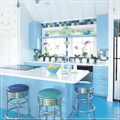 a blue and white kitchen with stools next to the counter top, sink and refrigerator