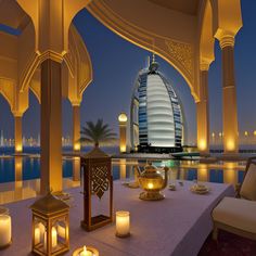 an outdoor dining area with lit candles and lights on the table in front of a view of burj al arab