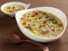 two white bowls filled with soup on top of a brown table next to spoons