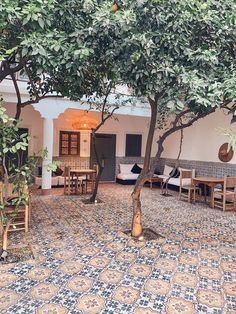 an outdoor seating area with tables and chairs under a tree in the middle of a courtyard