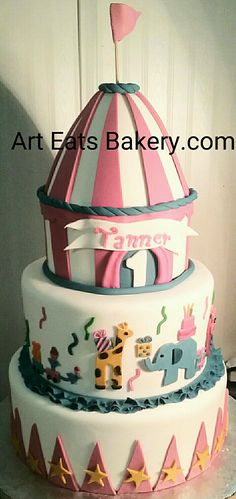 a three tiered cake with an elephant and circus theme on the top, sitting on a table in front of a white wall