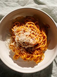 a white bowl filled with pasta covered in parmesan cheese on top of a table