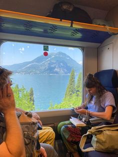 two people are sitting on a train looking out the window at mountains and blue water