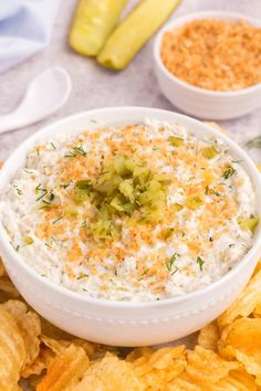 a white bowl filled with dip surrounded by chips and pickle slices on a table