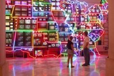 two people standing in front of a large display of television's on the wall