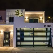 the front entrance to a modern house with lights on and an open gate at night