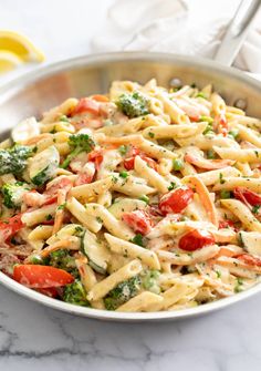 a pasta salad with tomatoes, broccoli and cheese in a skillet on a marble countertop