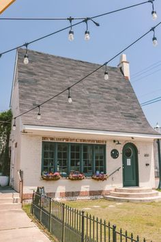 a small white house with green shutters and lights on the front door is surrounded by greenery