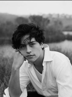 black and white photograph of a young man sitting in a field with his hands on his head