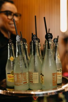 there are six bottles with drinking straws in them on a silver tray, and one is empty