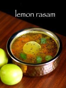 lemon rasam in a metal bowl next to two green apples on a wooden table