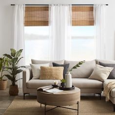 a living room filled with furniture and windows covered in white drapes next to a coffee table