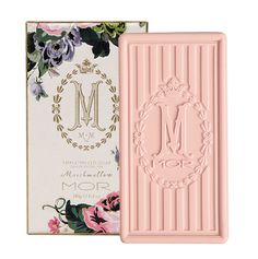 a pink soap bar next to a box with floral designs on it and the letter m