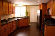 an empty kitchen with wood cabinets and black counter tops is seen in this image from the doorway