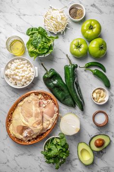 an assortment of vegetables and meats on a marble counter top, including green peppers, onions, avocado, garlic, tomatoes, cucumbers, and other ingredients