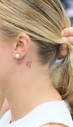 a woman with a small butterfly tattoo on her left side behind her ear, while she is wearing a white top