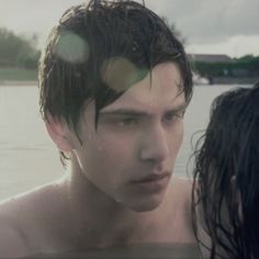 a man with wet hair standing next to a woman in the water looking at him