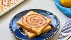 two slices of cinnamon roll on a blue plate next to a baking pan and lemons