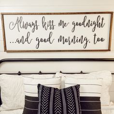 a bed with black and white pillows and a framed sign above it that says, always kiss me goodnight and good morning too