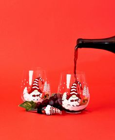 red wine being poured into two glasses with santa hats on them and candy canes