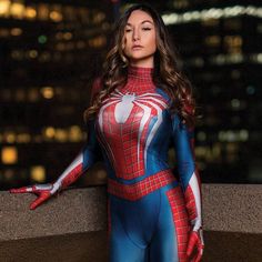 a woman in a spider - man costume poses for a photo at night with the city lights behind her