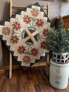 a potted plant sitting on top of a wooden chair next to a quilted wall hanging