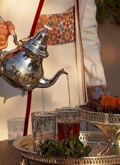 a person pouring water into a teapot on top of a tray with silver cups