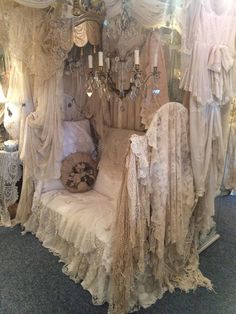 an old fashioned bed with lace on it and chandelier hanging from the ceiling