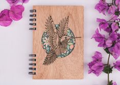 a wooden notebook with an image of a bird on it next to some purple flowers