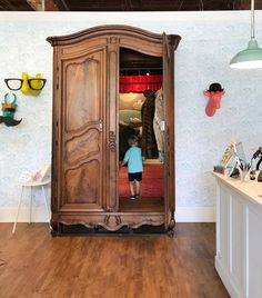 a little boy standing in front of a wooden armoire