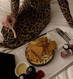 a person sitting on a bed with some food in front of them and condiments to the side