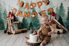 a baby boy sitting on the floor with a cake in front of him and decorations behind him