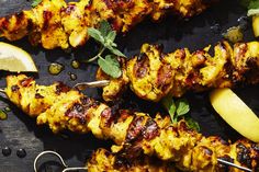 several skewers of food on a table with lemon wedges and mint garnish