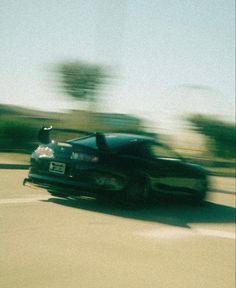 a black car driving down the road with trees in the backgrouund and blurry behind it