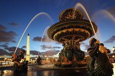 the fountain is lit up at night with water shooting out from it's sides