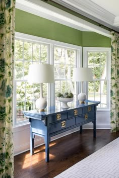 a blue table with two lamps sitting on top of it next to a window covered in curtains