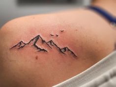 a woman's shoulder with a mountain tattoo on her left arm and birds flying over it