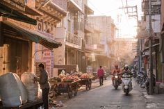 people are walking down the street in an old city with many buildings and shops on either side