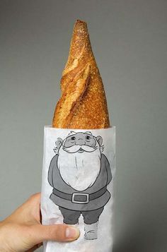 a hand holding a baguette wrapped in paper with an image of santa claus on it