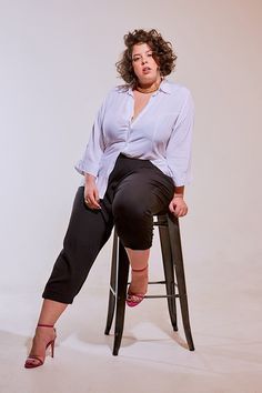 a woman sitting on a stool posing for the camera with her hands in her pockets