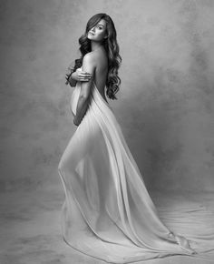 a woman in a long white dress posing for a black and white photo with her hands on her hips