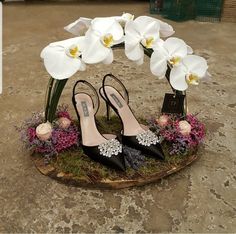 a pair of black high heeled shoes sitting on top of a wooden stand with flowers