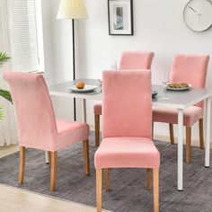 a dining room table with pink chairs and a white clock on the wall behind it