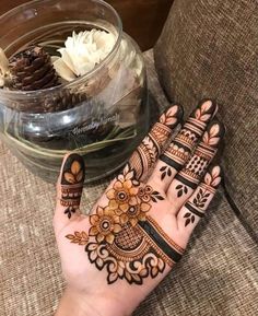 a person's hand with henna tattoos on it and flowers in the background