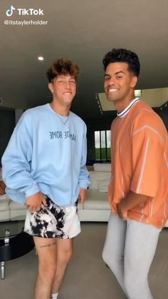 two young men standing next to each other in front of a living room with couches