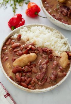 two bowls filled with beans and rice on top of a white tablecloth next to red peppers